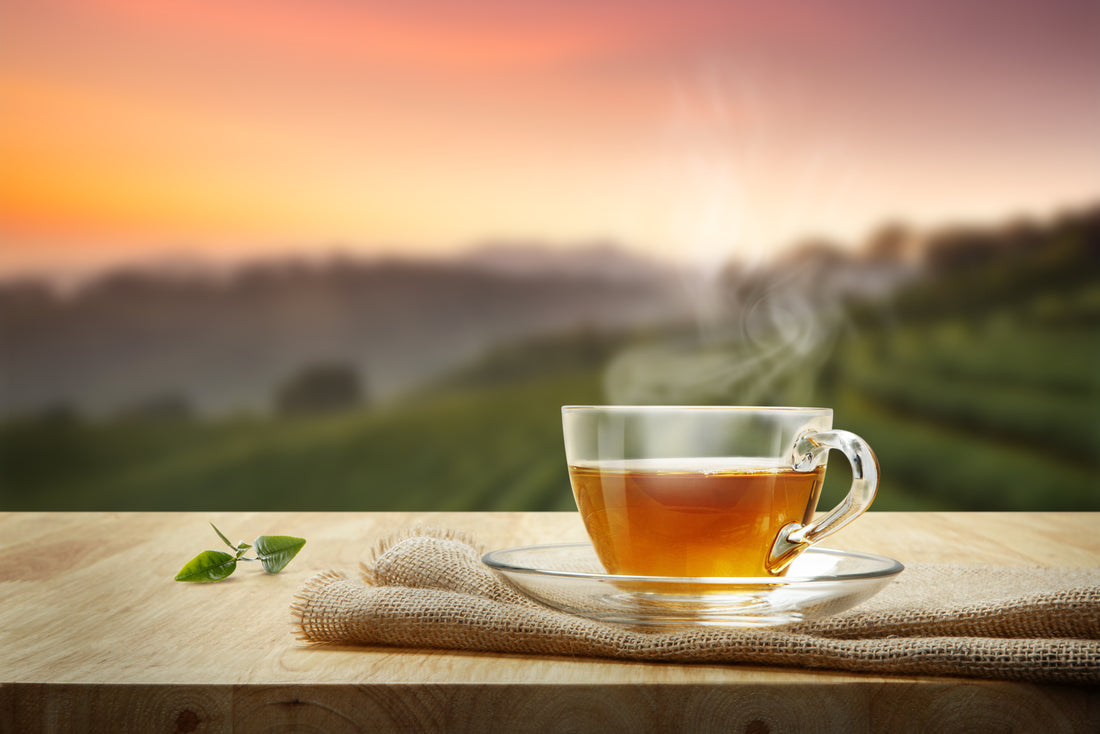 Tasse Tee auf einem Holztisch, im Hintergrund sind Weinberge, sowie der Sonnenuntergang zu sehen.