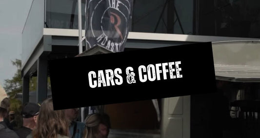 Besucher vor dem Kaffeemobil von THE ROASTERY by Caffè Passione beim 3. Cars & Coffee Event, mit markantem ‚Cars & Coffee‘-Schriftzug im Vordergrund und THE ROASTERY Flagge im Hintergrund.
