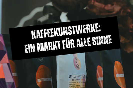 Kaffeebeutel von THEROASTERY by Caffè Passione auf einem Holztisch, darüber ein Banner mit der Aufschrift: „KAFFEEKUNSTWERKE – Ein Mart für alle Sinne“.