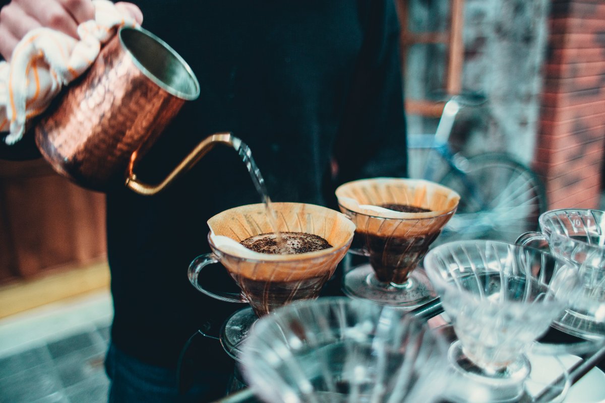 Person gießt heißes Wasser über Kaffeekanne, auf der sich ein Kaffeefilter mit gemahlenen Kaffeebohnen befindet