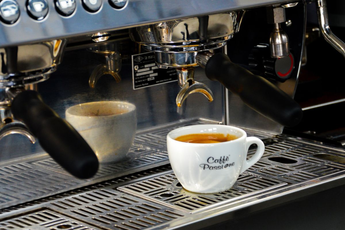 Espresso in einer Tasse von Caffè Passione mit goldener Crema, platziert vor einer silberfarbenen Siebträgermaschine in einer modernen Barista-Umgebung.