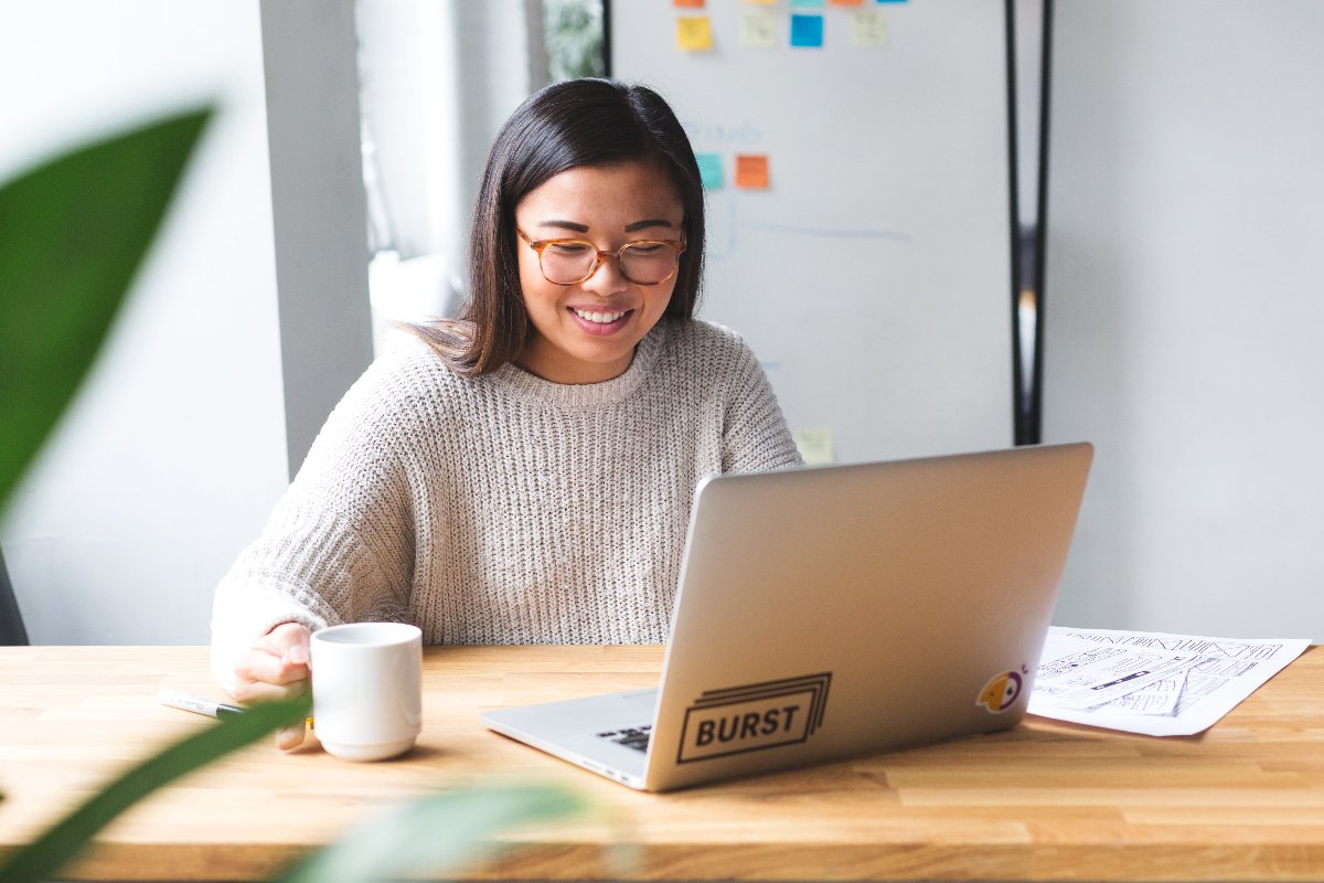 Person, die vor dem Laptop sitzt und eine Tasse Kaffee in der Hand hält