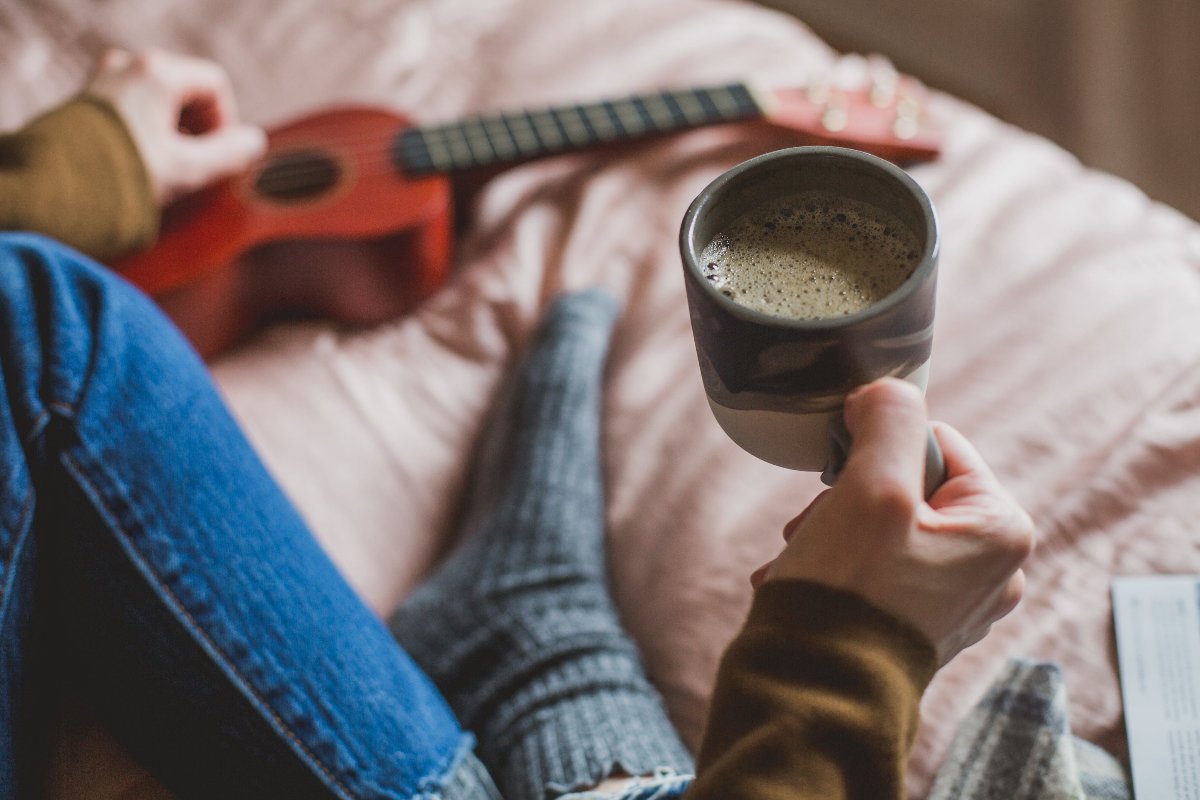 Kaffeetasse mit Kaffee, die von einer Person im Bett gehalten wird