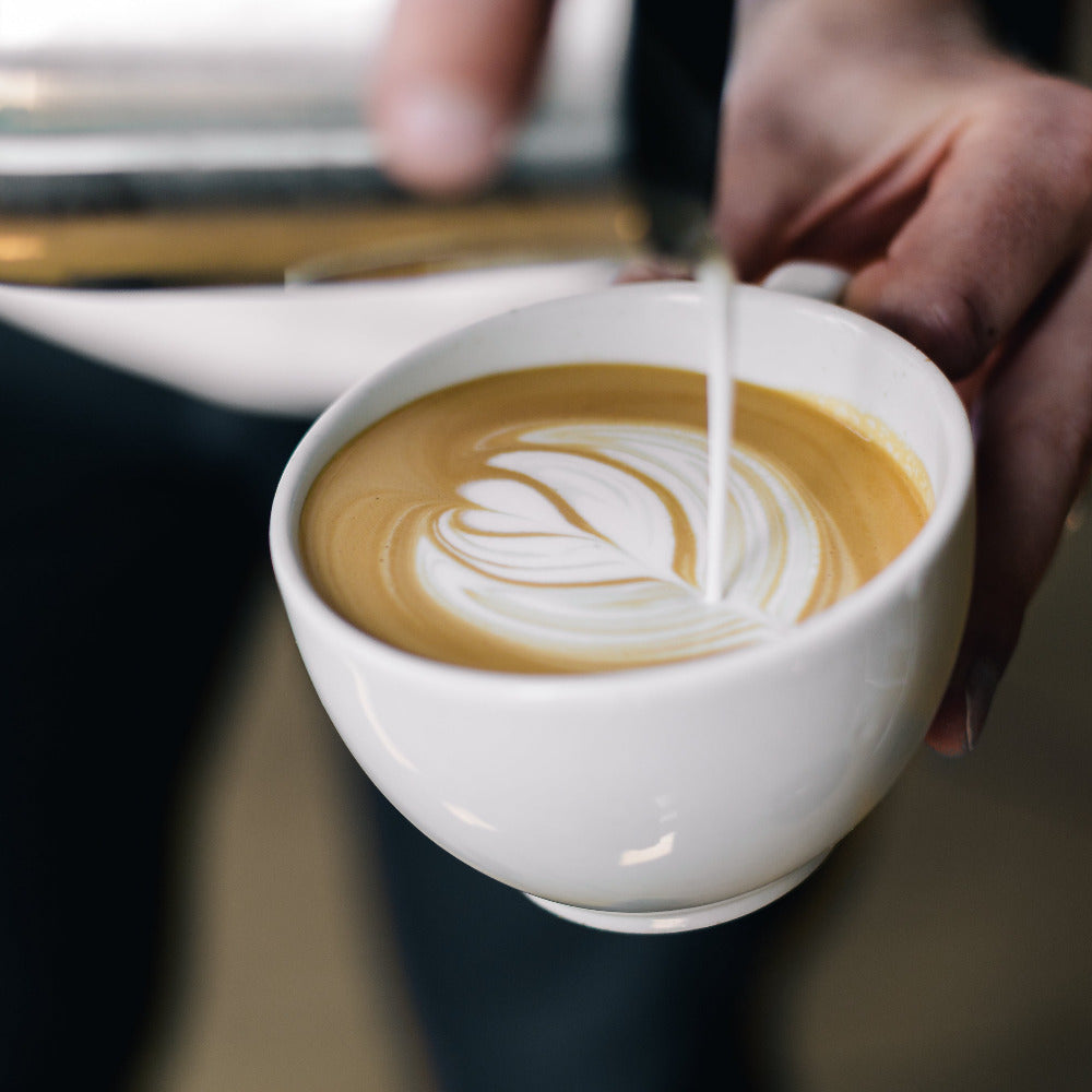 Barista gießt Milchschaum in eine Tasse Cappuccino und formt Latte Art.