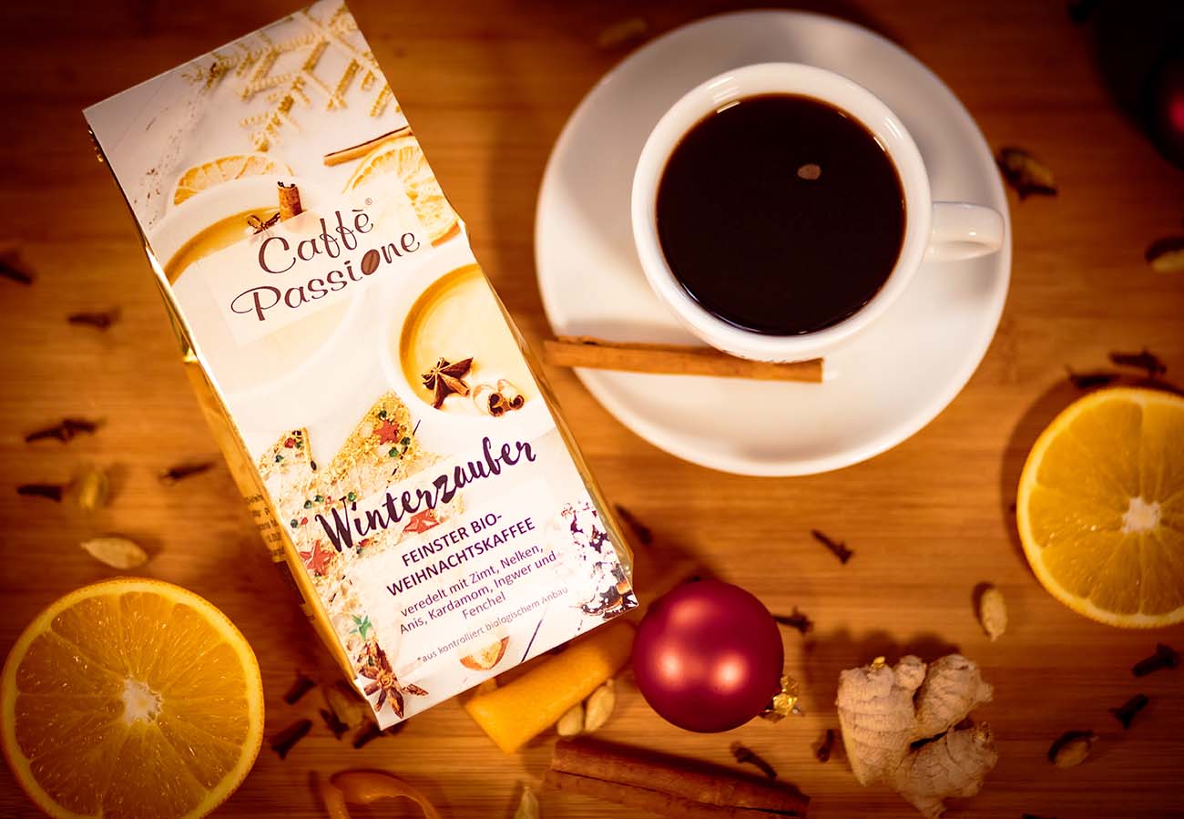 Verpackung der Kaffeesorte "Winterzauber" mit aufgeschnittenen Orangen und einer heißen Tasse Kaffee, alles auf einen Holztisch